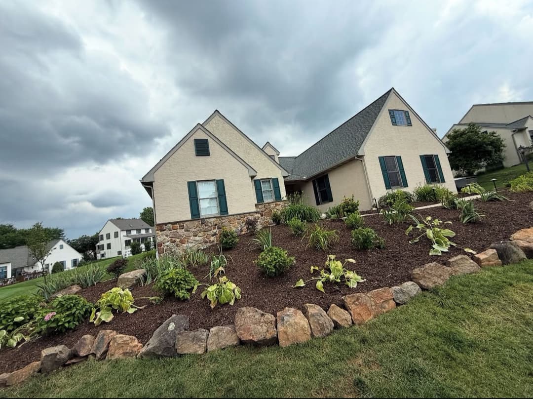 Charming house with landscaped garden and stone border under a cloudy sky.