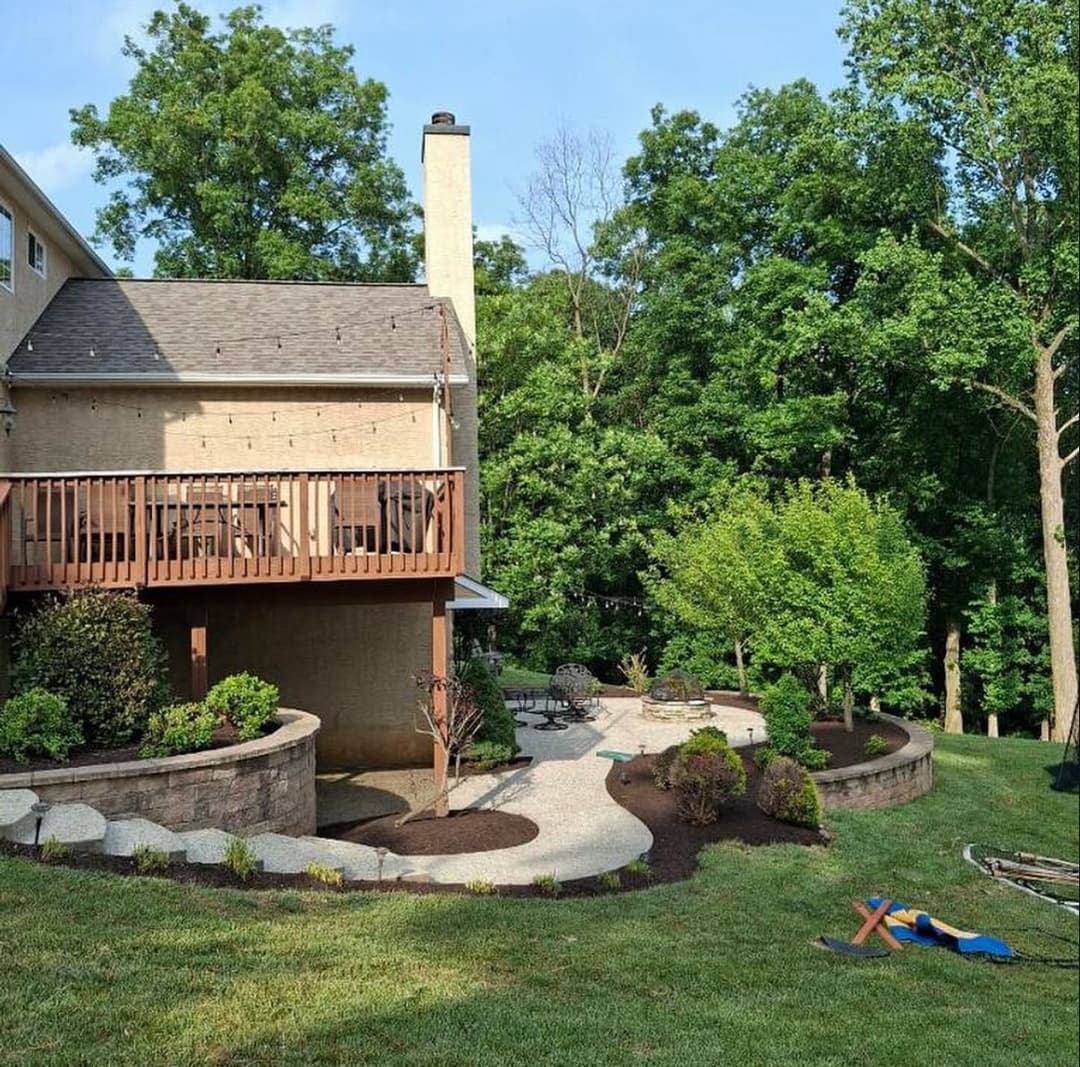 Backyard landscape featuring a deck, stone path, and lush greenery in a residential setting.
