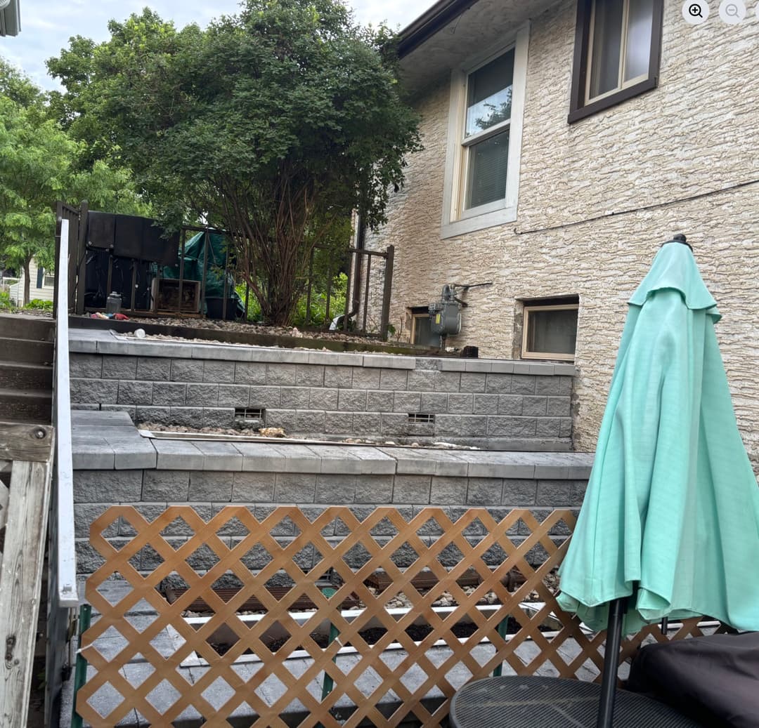 Backyard patio with stone landscaping, BBQ area, and green umbrella for outdoor seating.