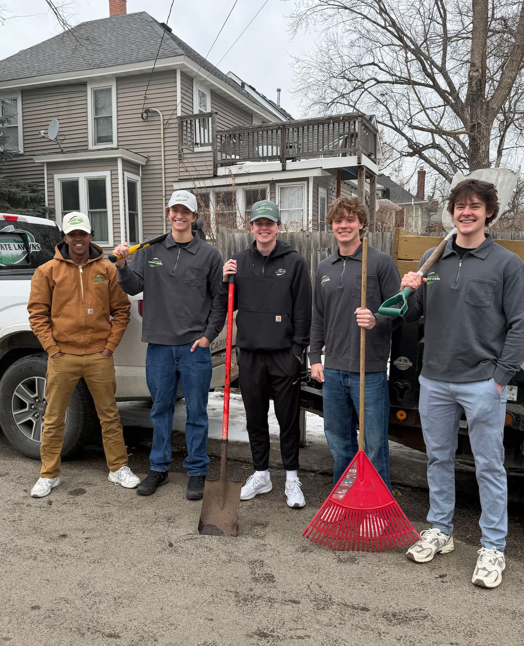 Group of five young men holding gardening tools in front of a truck, ready for landscaping work.