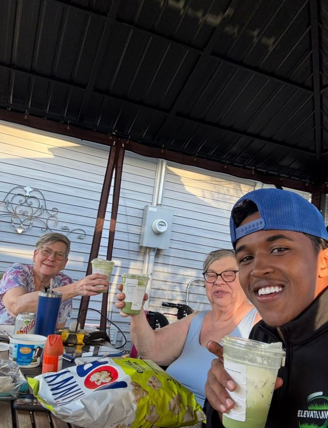 Three friends enjoying green drinks on a patio, smiling and raising their glasses.