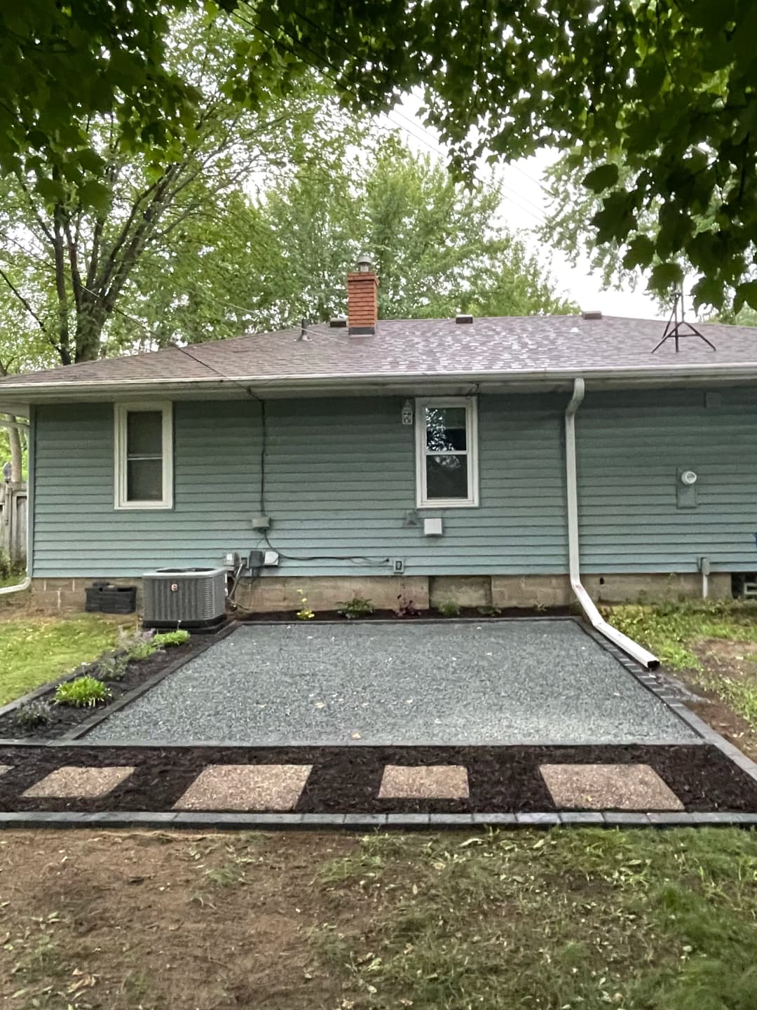 Backyard renovation featuring gravel area and decorative stone pathway beside blue home.