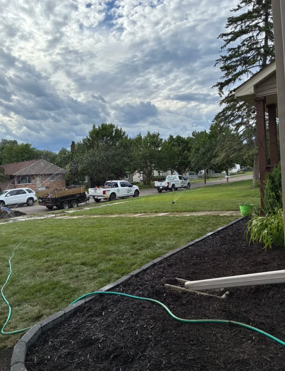 Landscaped front yard with vehicles parked on the street and cloudy sky overhead.