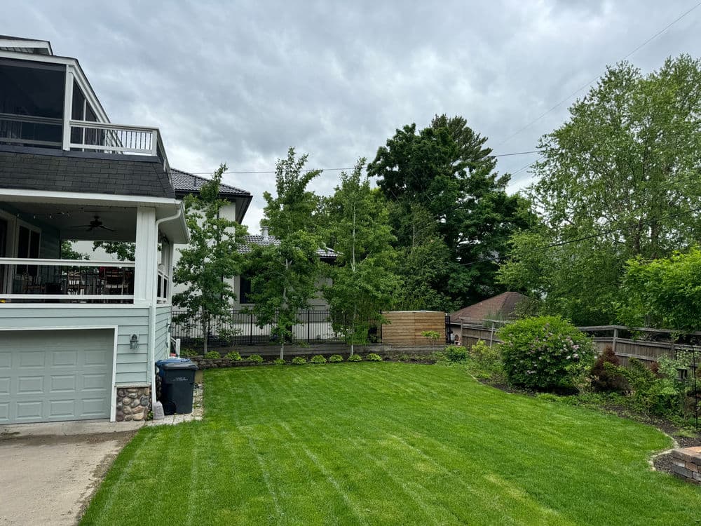 Modern home with landscaped yard, green grass, and trees under a cloudy sky.