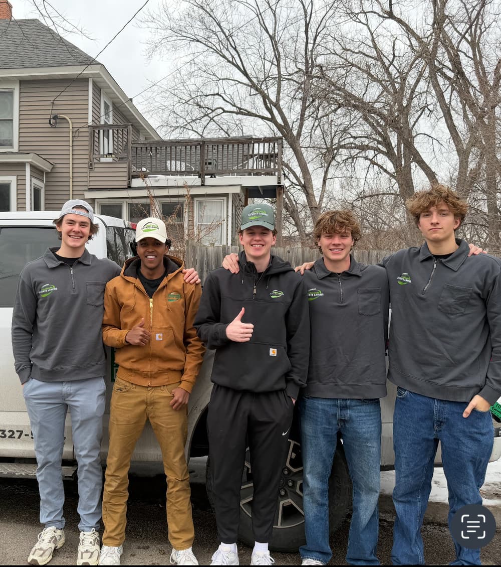 Group of five young men in branded jackets posing outdoors by a white vehicle.
