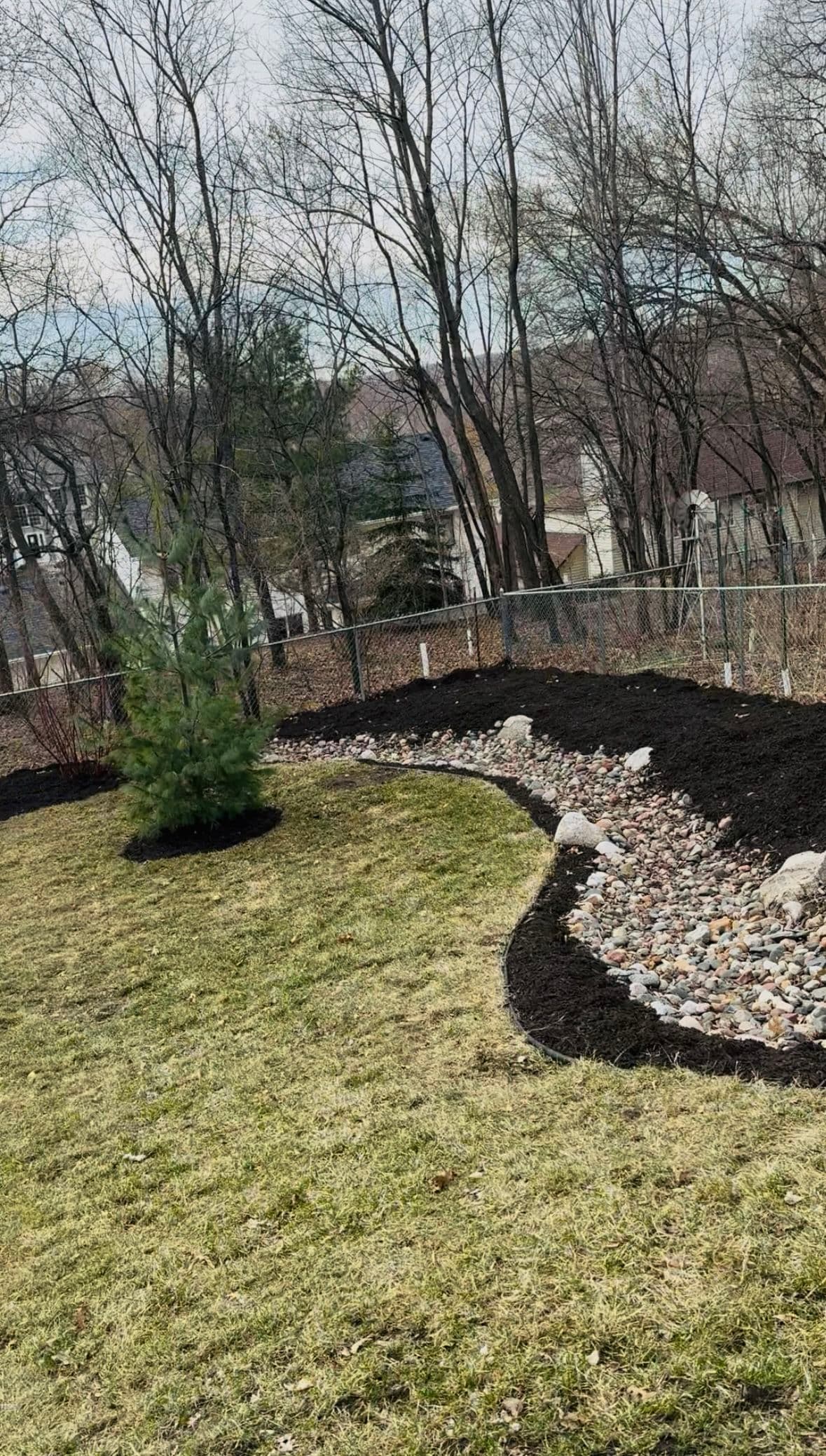 Fresh Mulch, River Rocks, and Young Trees Planted in One Backyard image